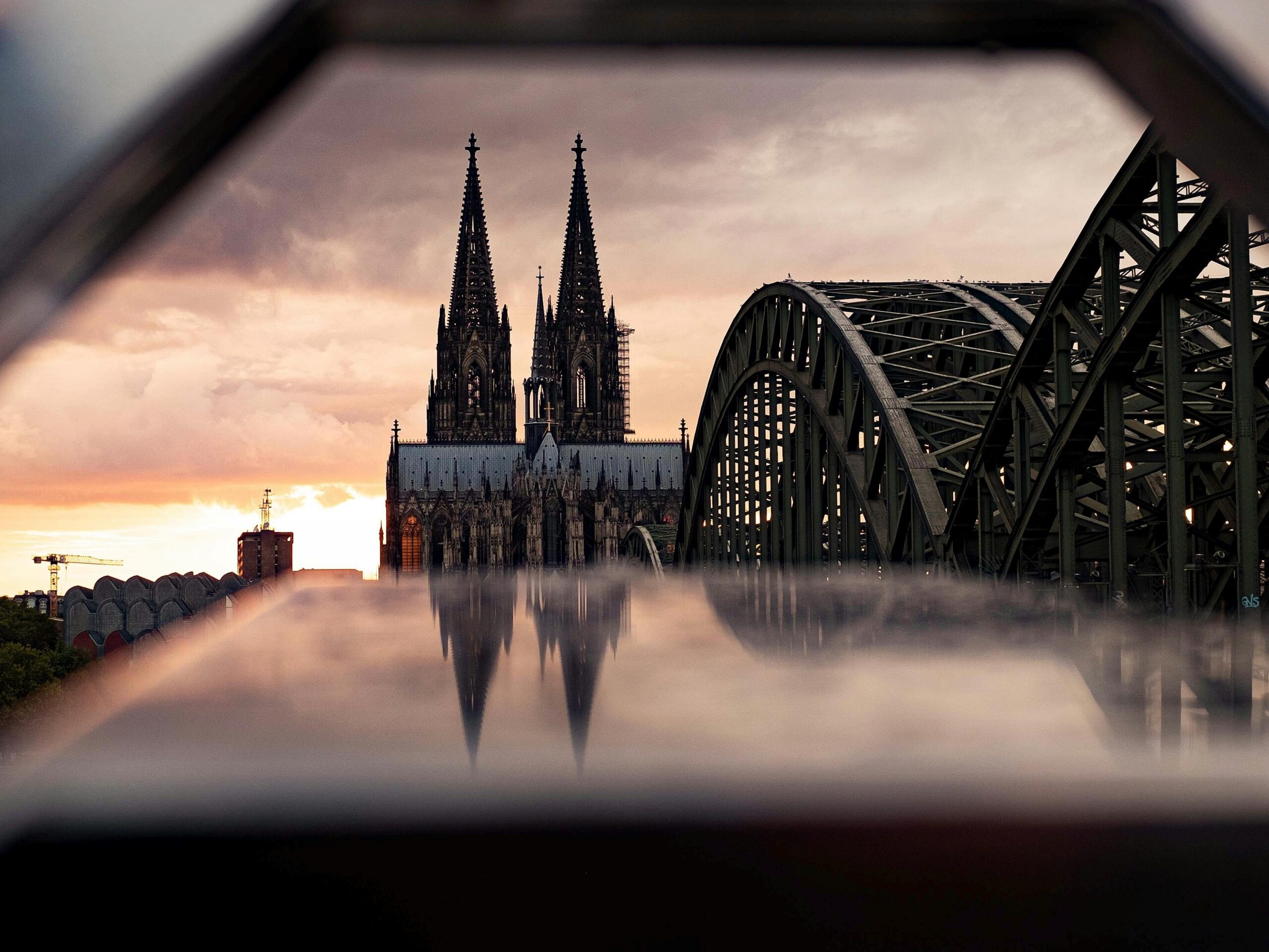 Majestic view of Cologne Cathedral and Hohenzollern Bridge at sunset, capturing gothic architecture.